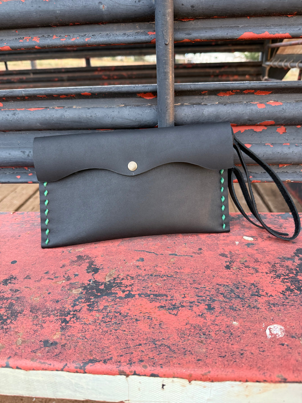 Black leather clutch bag with green stitching on 