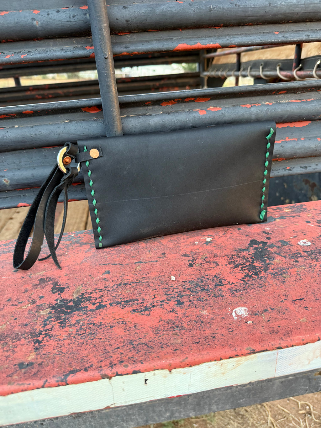 Black leather clutch with green stitching on a red and gray surface