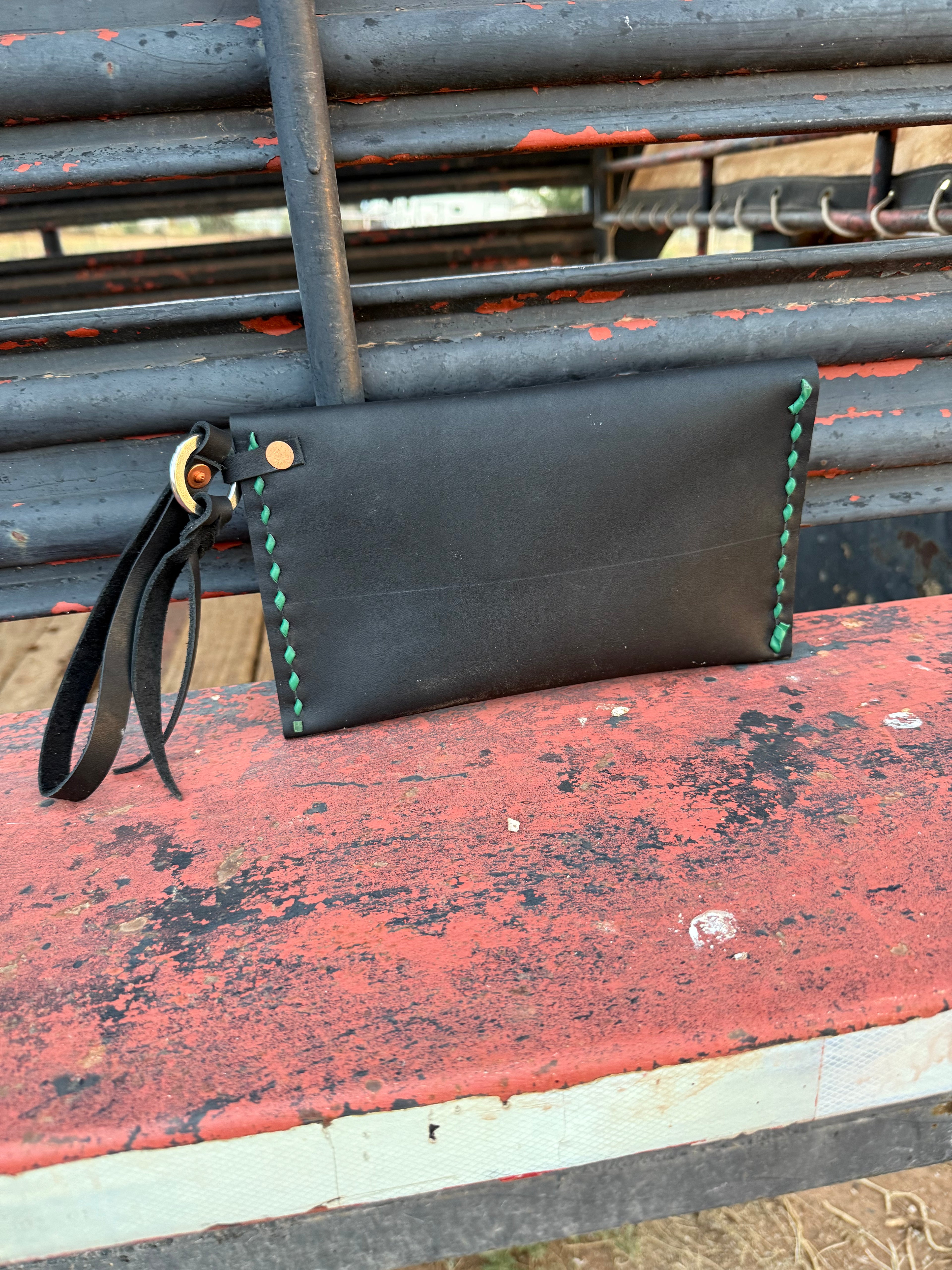 Black leather clutch with green stitching on a red and gray surface