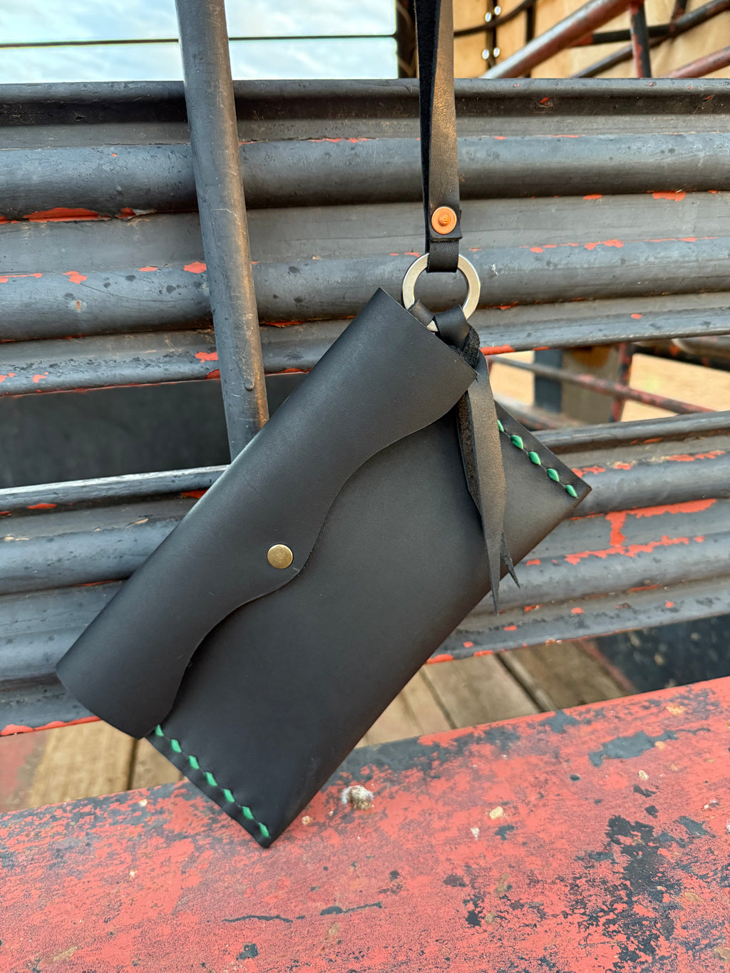 Black leather clutch bag with a strap on a metal surface
