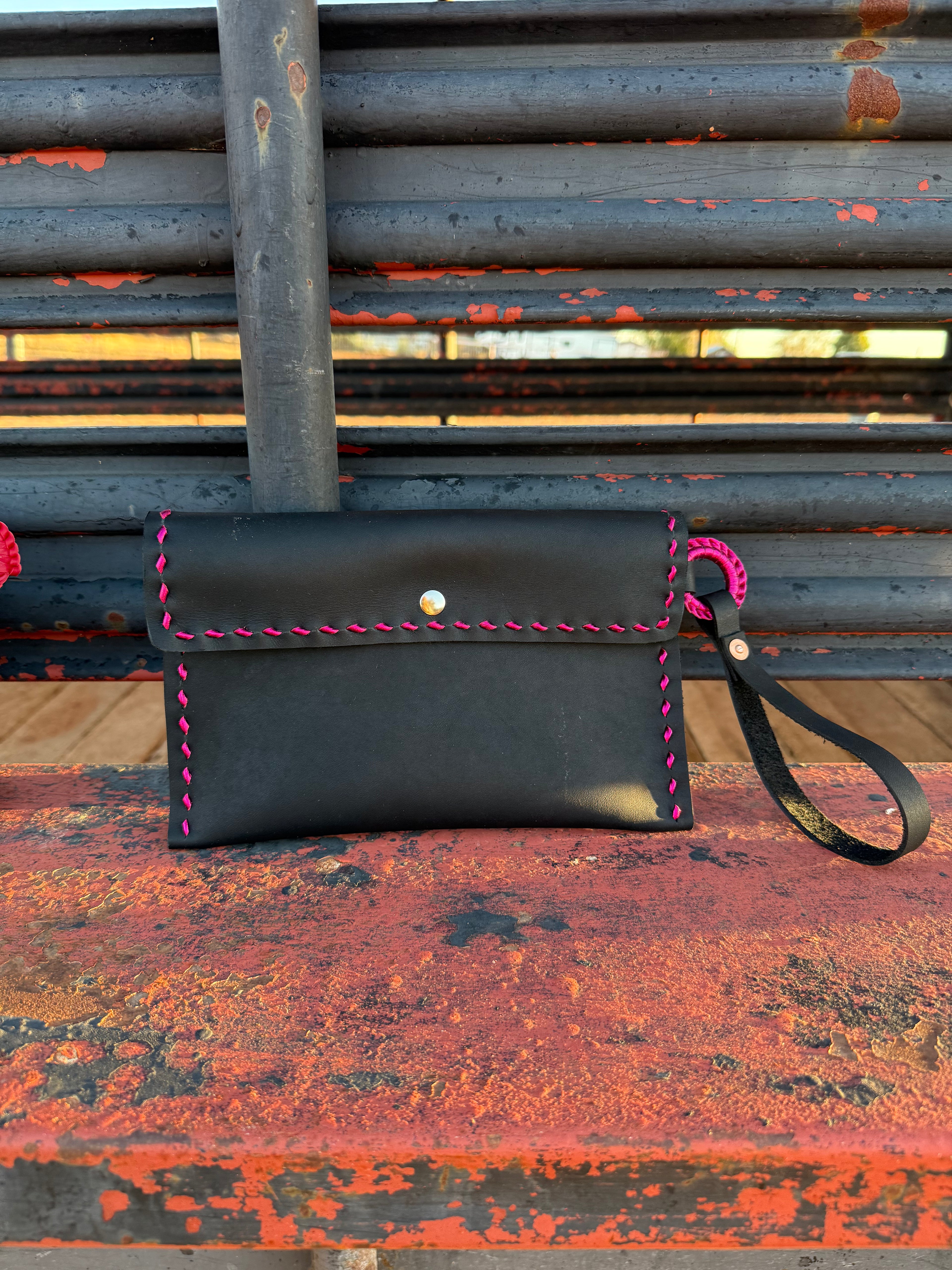 Black leather clutch with pink stitching on a rusty metal surface